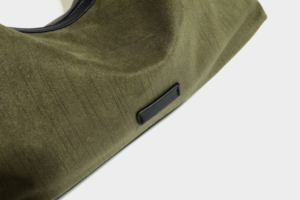 Slouchy olive green canvas hobo shoulder bag with black leather-look trim, zip-top closure, and adjustable strap, detail view