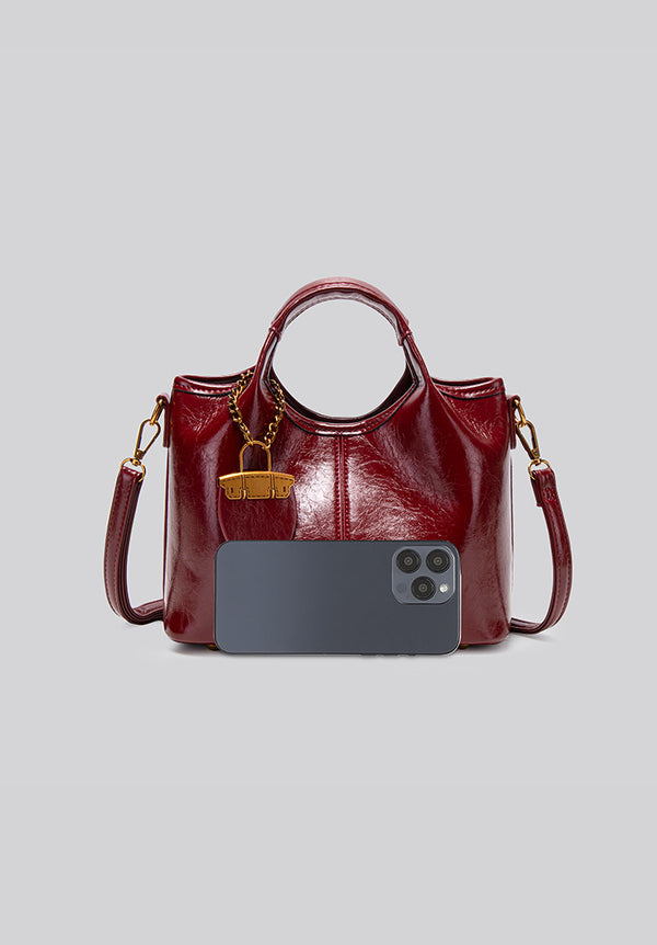 Structured crinkle-gloss top-handle satchel in deep burgundy with antique gold lock charm and detachable shoulder strap