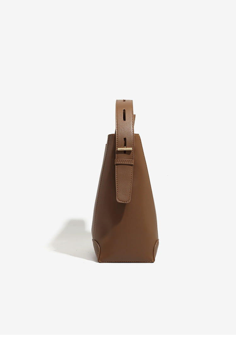 Structured smooth leather-look bucket shoulder bag with long adjustable strap and gold-tone buckle hardware in brown, detail