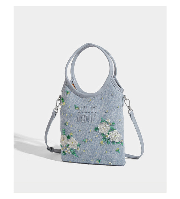 Kleine hellblaue Mini-Tote-Bag aus Stoff mit weißer Perlenblumenverzierung, runden Henkeln, silberfarbenen Beschlägen und