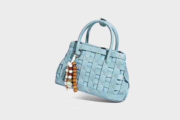 Small structured woven satchel tote with rounded top handles, silver-tone ring hardware, and bead tassel charm, detail view