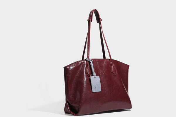 Übergroße, weich fallende Tote-Bag in dunklem Bordeauxrot mit glänzender, geknautschter Lederoptik, zwei langen Schulterriemen und Kontrast