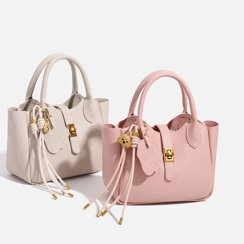 Small structured pebbled leather-look mini tote bag with gold-tone hardware, front toggle closure, knotted bear tassel charm