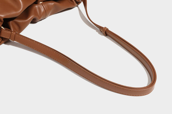 Slouchy ruched drawstring shoulder bag in smooth leather-look finish with gold-tone emblem and slim adjustable strap, detail