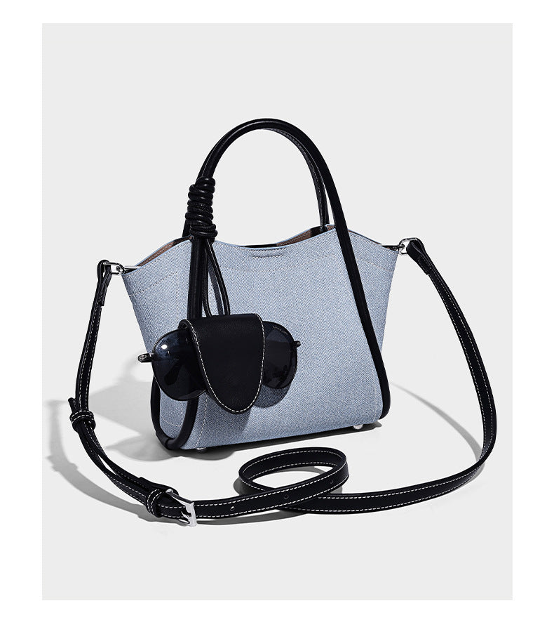 Structured canvas tote bag with knotted top handles, leather-look black trim, front flap pocket, and pink tulip flower charm
