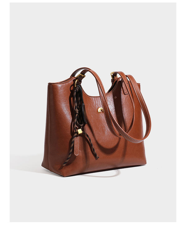 Structured smooth leather-look tote bag with long shoulder strap, gold-tone hardware, and hanging tassel-coin charm, detail