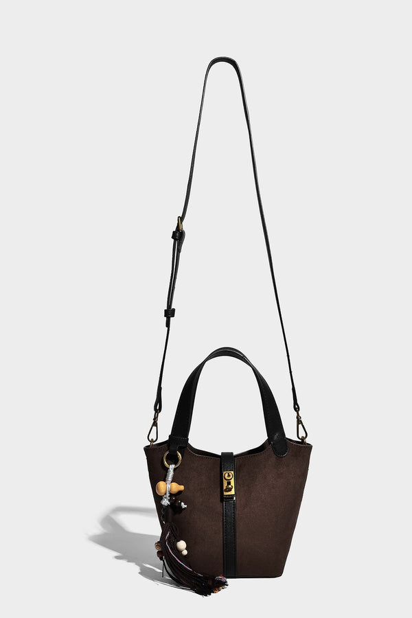 Small structured trapezoid tote bag in matte suede-look finish with black contrast trim, gold-tone front clasp, tassel charm