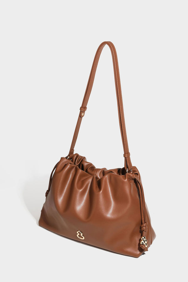 Slouchy ruched drawstring shoulder bag in smooth leather-look finish with gold-tone emblem and slim adjustable strap, detail