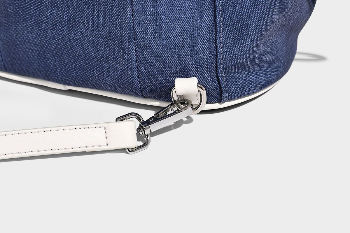 Compact denim drawstring backpack with white leather-look piping, flap-top buckle closure, front zip pocket, and silver-tone