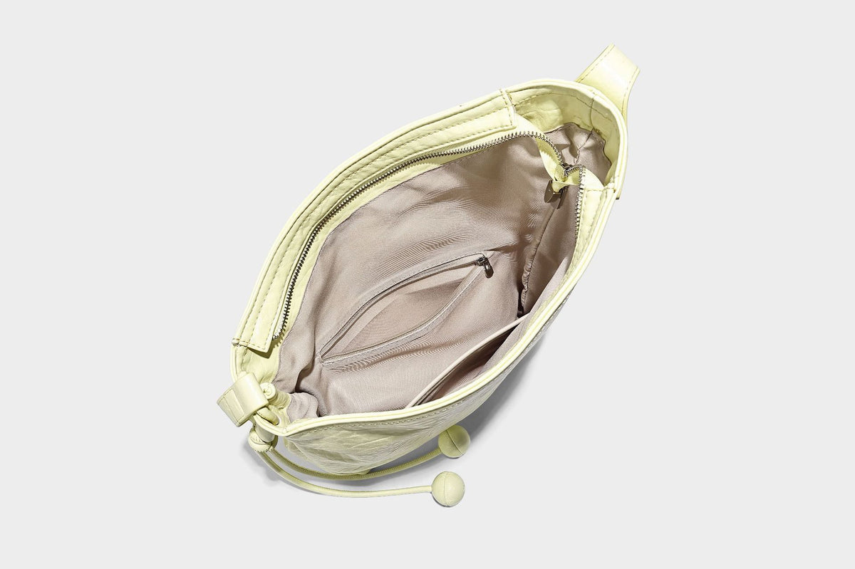 Slouchy hobo shoulder bag in pale yellow with slim strap, drawstring bead closure, and pink tulip floral charm, detail view