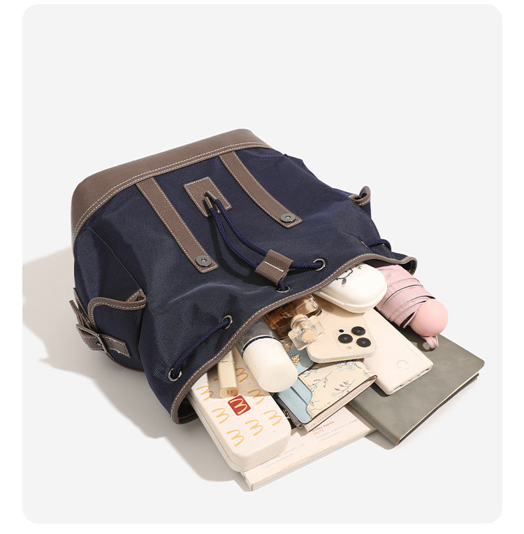 Deep navy canvas backpack with brown textured leather-look trim, drawstring flap closure, buckle-strap front detail, and