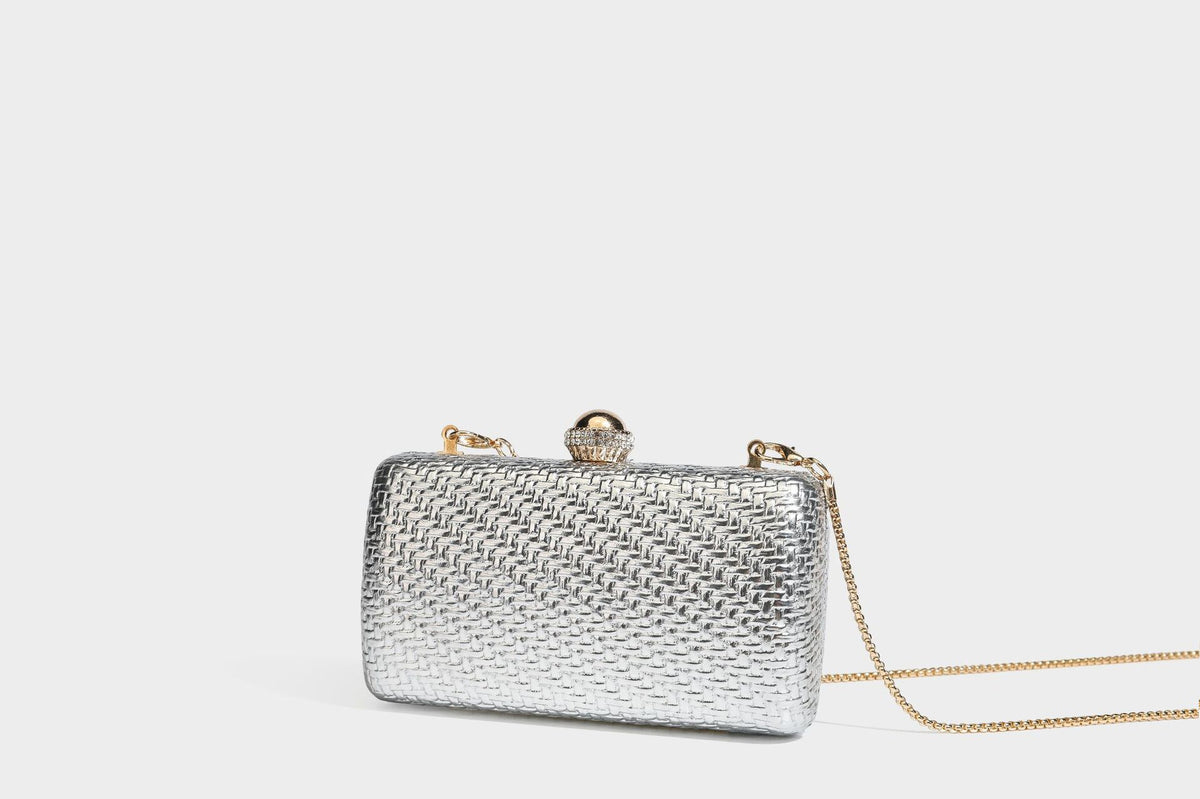 Small structured metallic woven-texture box clutch bag with jeweled kiss-lock dome clasp and slim gold chain strap, detail