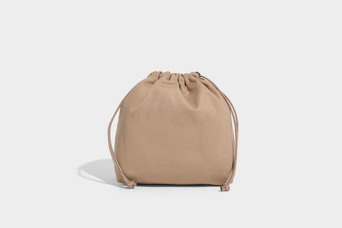 Two-tone open-weave tote bag in beige and cream with brown leather-look handles, tassel bead charm, and detachable