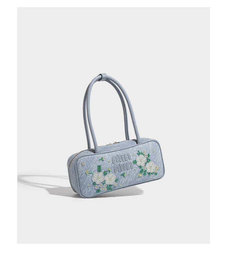 Small structured light blue denim-texture bowling bag with white floral bead embroidery, dual rounded top handles, and