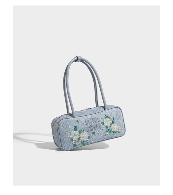 Small structured light blue denim-texture bowling bag with white floral bead embroidery, dual rounded top handles, and