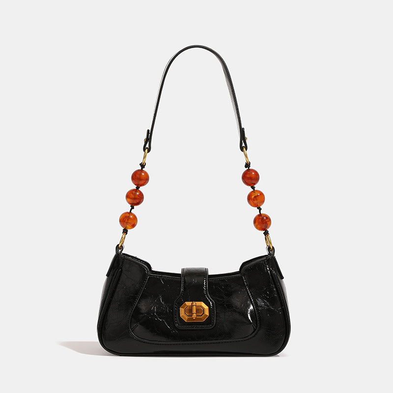 Compact glossy crinkled baguette shoulder bag with amber resin bead strap accent and gold-tone turn-lock closure, detail view