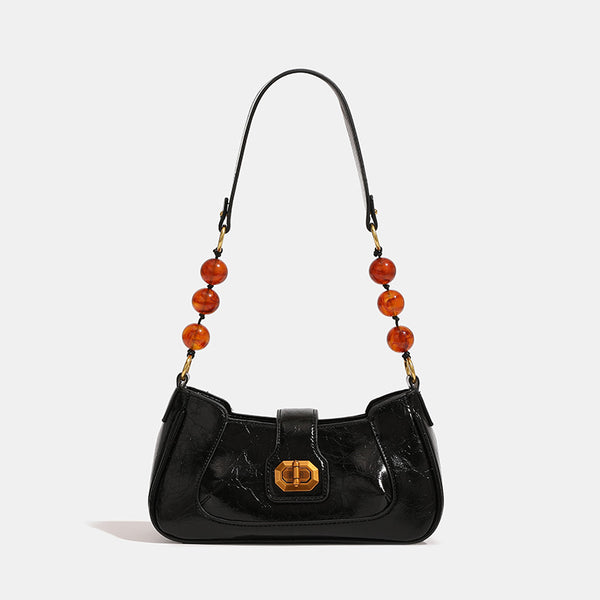 Compact glossy crinkled baguette shoulder bag with amber resin bead strap accent and gold-tone turn-lock closure, detail view