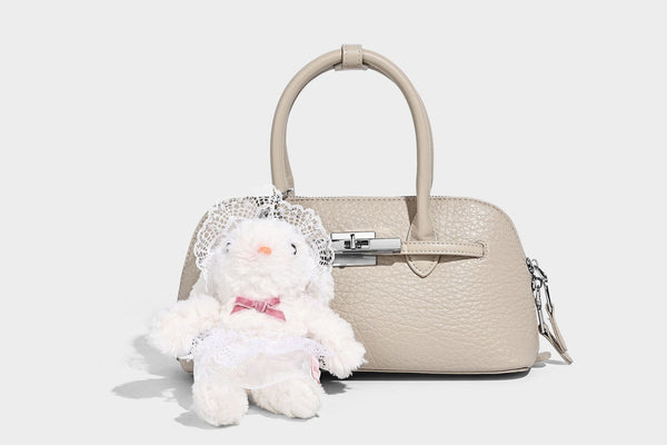 Small structured shell-silhouette top-handle bag with pebbled leather-look finish, silver-tone turn-lock hardware, and