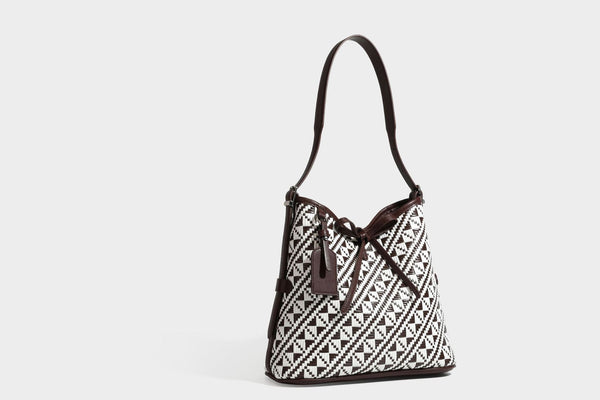Woven geometric bucket shoulder bag in white and dark brown two-tone pattern with leather-look trim and drawstring top