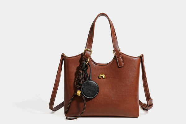 Structured smooth leather-look tote bag with long shoulder strap, gold-tone hardware, and hanging tassel-coin charm, detail