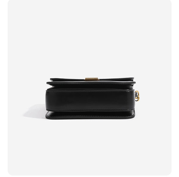 Mini structured black flap crossbody bag with gold-tone ribbed rectangular clasp and adjustable shoulder strap, detail view