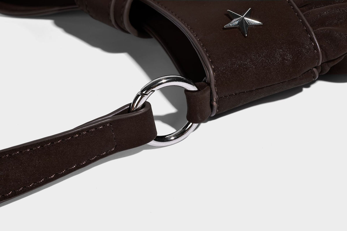 Ruched shoulder bag with curved flap, silver star studs, dangling starfish charm, and adjustable crossbody strap, detail view