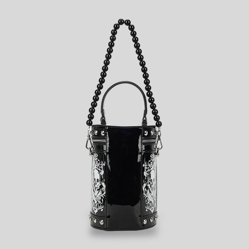 Schwarze glänzende zylindrische Barrel-Bag mit weißen Totenkopf-Blumen-Prints, silberfarbenen Pyramidennieten, schwarzem Perlenhenkel und