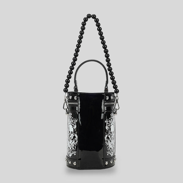Black glossy cylindrical barrel bag with white skull-floral print panels, silver pyramid studs, black beaded top handle, and