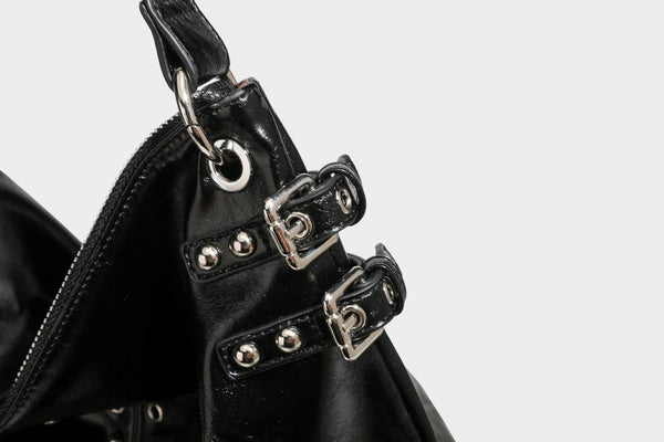 Black glossy leather-look slouchy shoulder bag with silver stud and eyelet hardware, top zip closure, front zip pocket, and