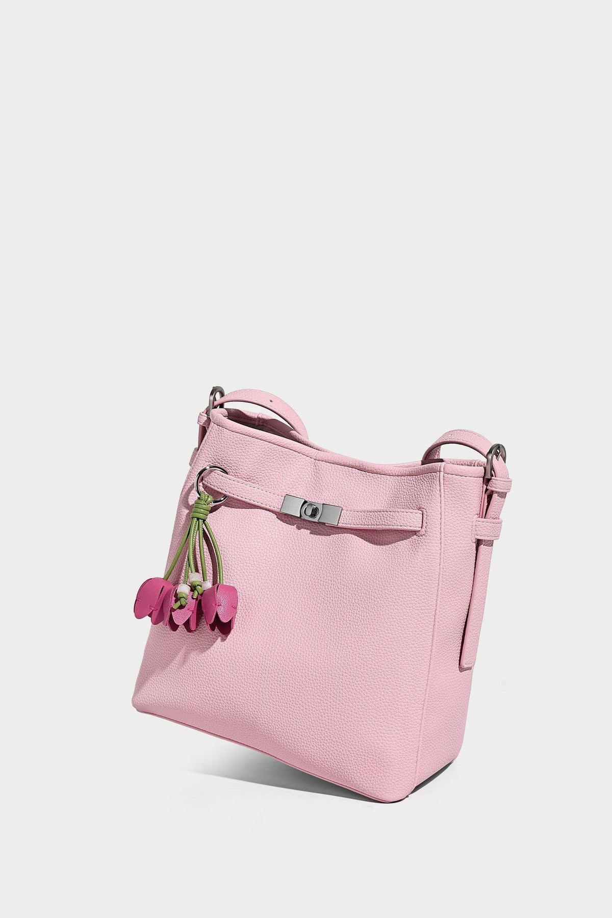 Soft-structured pebbled bucket shoulder bag with front turn-lock strap detail, adjustable strap, and hanging floral tassel