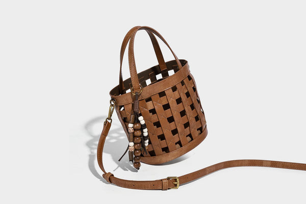 Small woven lattice bucket bag in brown leather-look finish with beaded tassel charm, dual top handles, and detachable