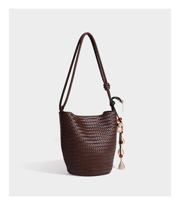 Olive green woven leather-look bucket bag with braided crossbody strap, knotted adjustment, and gold-tone tassel charm with