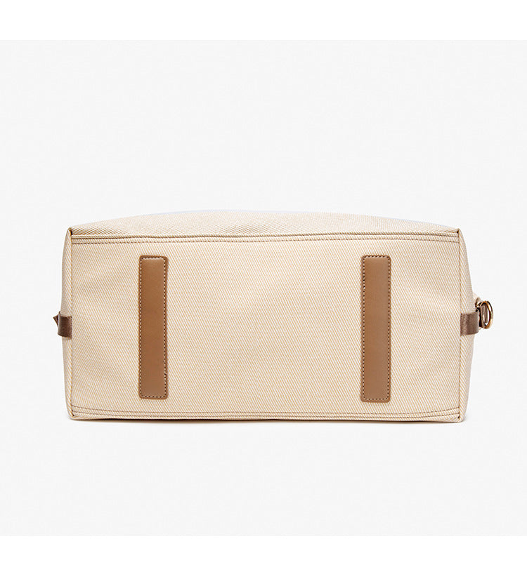 Structured woven duffel bag with dual tan webbing handles, detachable shoulder strap, top zip closure, and gold-tone