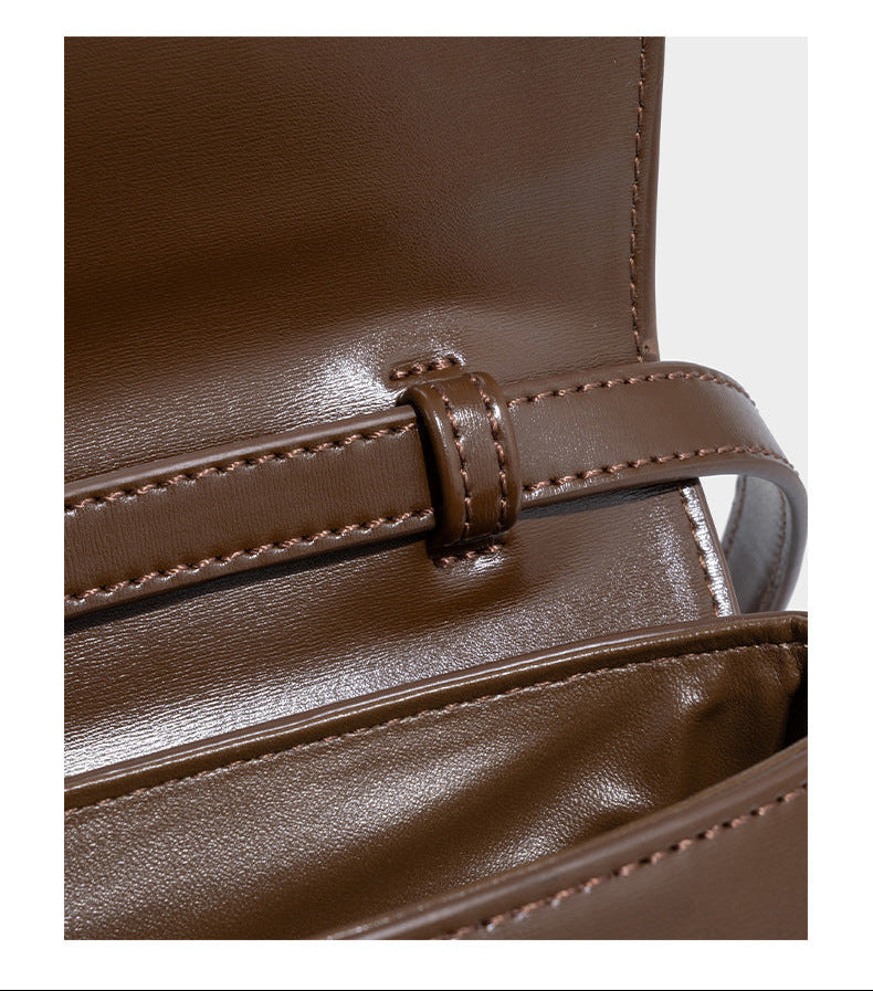 Small structured saddle bag with glossy leather-look finish, angular flap front, silver-tone metal clasp, and slim