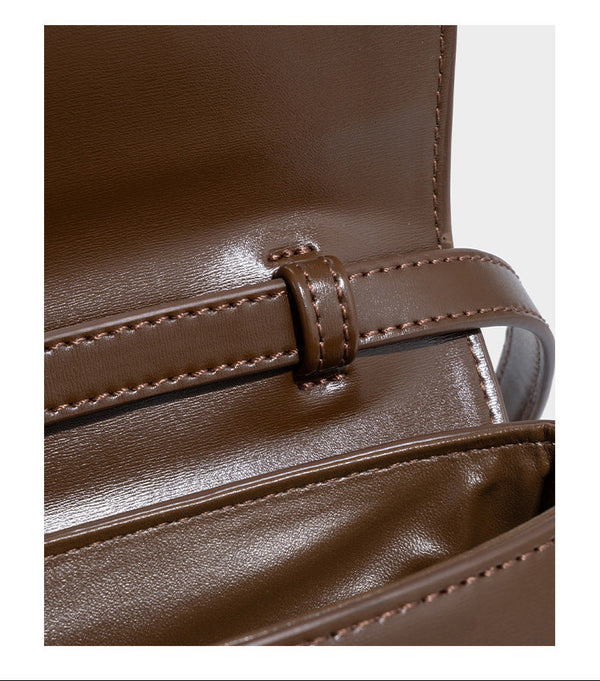 Small structured saddle bag with glossy leather-look finish, angular flap front, silver-tone metal clasp, and slim