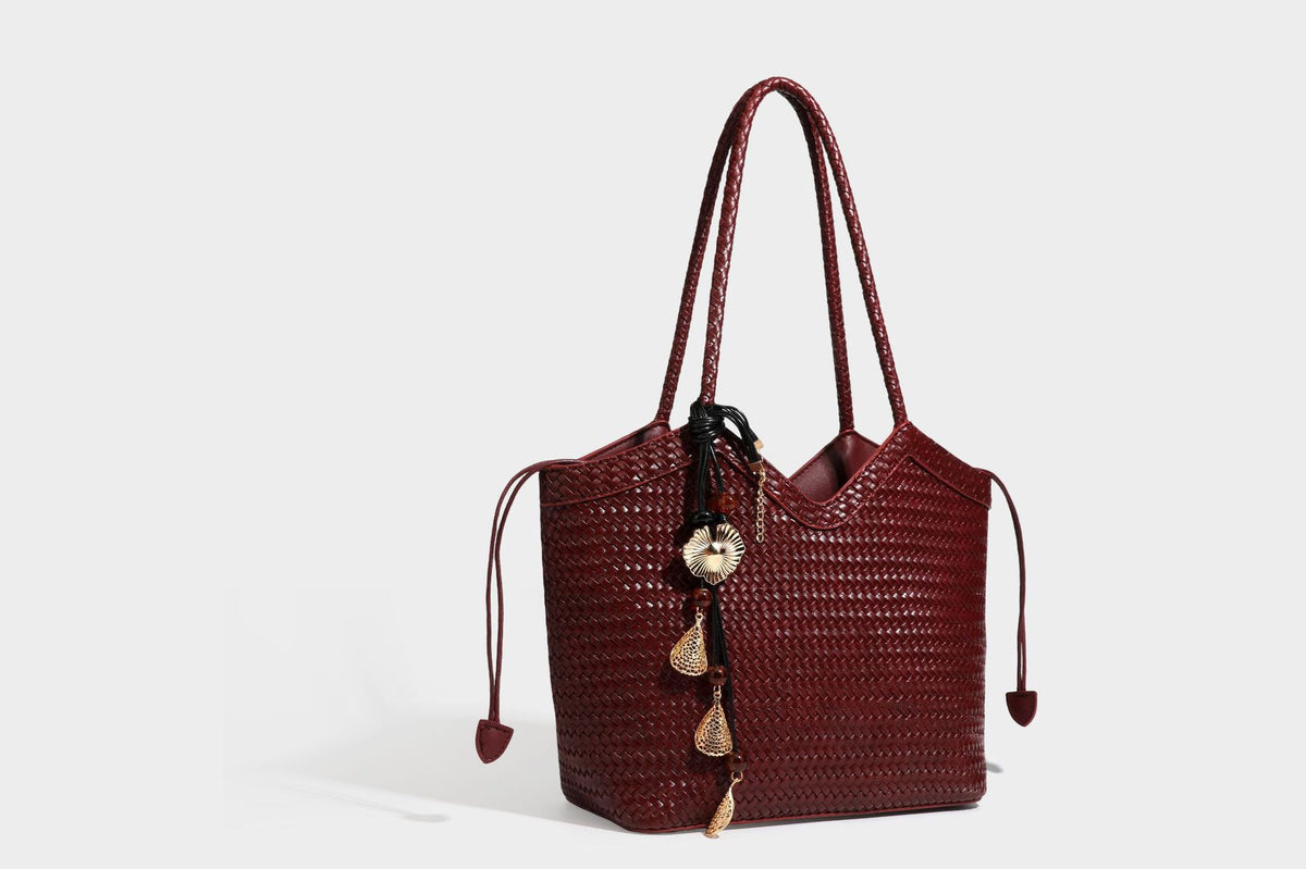 Olivgrüne Tote-Bag in Korbgeflecht-Optik mit dunkelbraunen geflochtenen Schulterriemen, seitlichen Kordelzügen und Perlenanhänger in Goldoptik