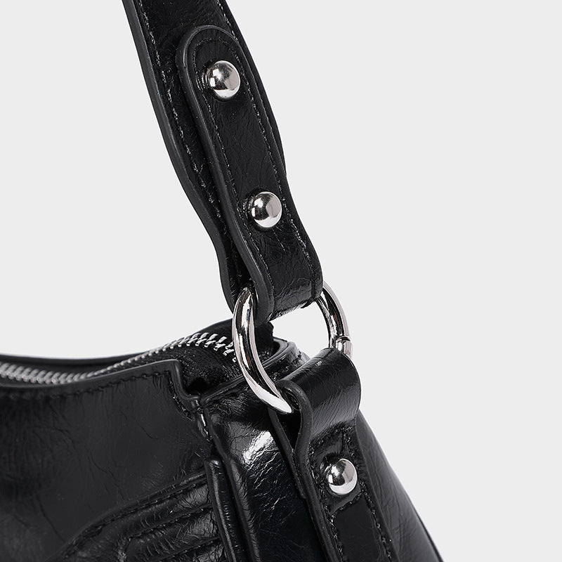Compact moto-inspired shoulder bag with crisscross grommet strap detail, glossy textured finish, and adjustable crossbody