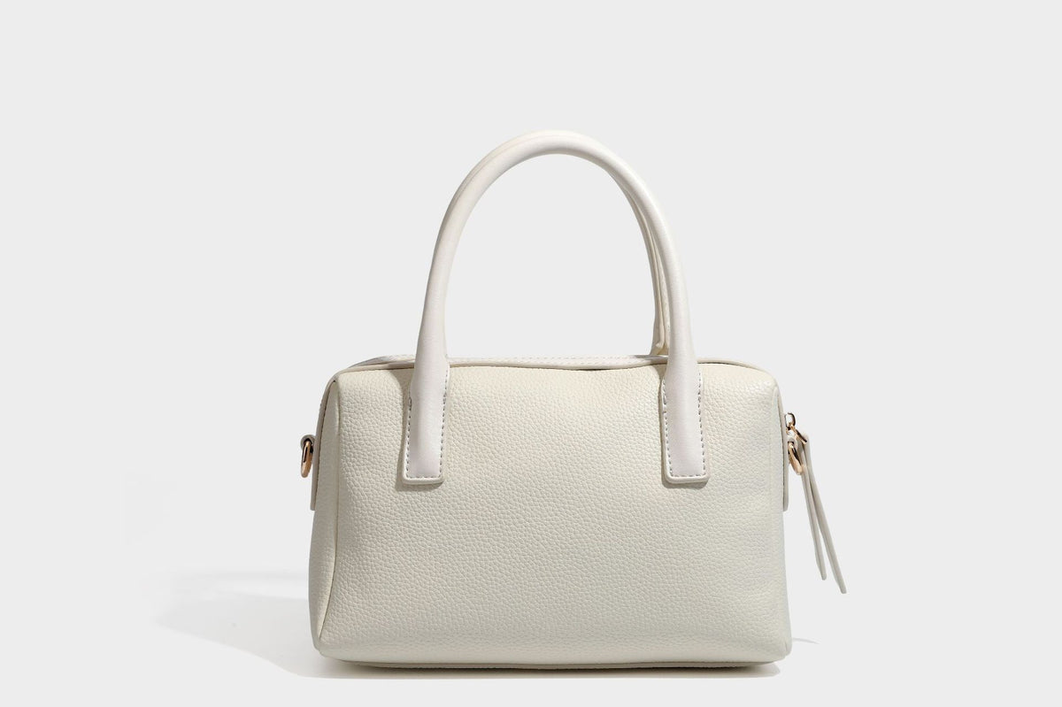 Small structured pillow satchel bag with pebbled leather-look finish, dual rolled top handles, gold-tone gourd emblem, and