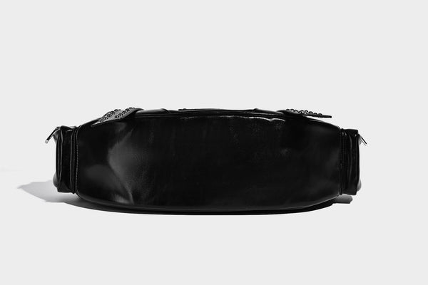 Glossy black crescent shoulder bag with silver-tone rivets, multiple zip pockets, and long adjustable studded straps, detail
