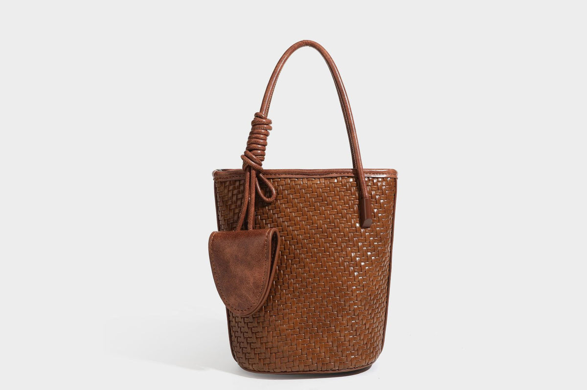 Structured woven-texture leather-look bucket bag in brown with knotted top handles, small front flap pouch, and adjustable