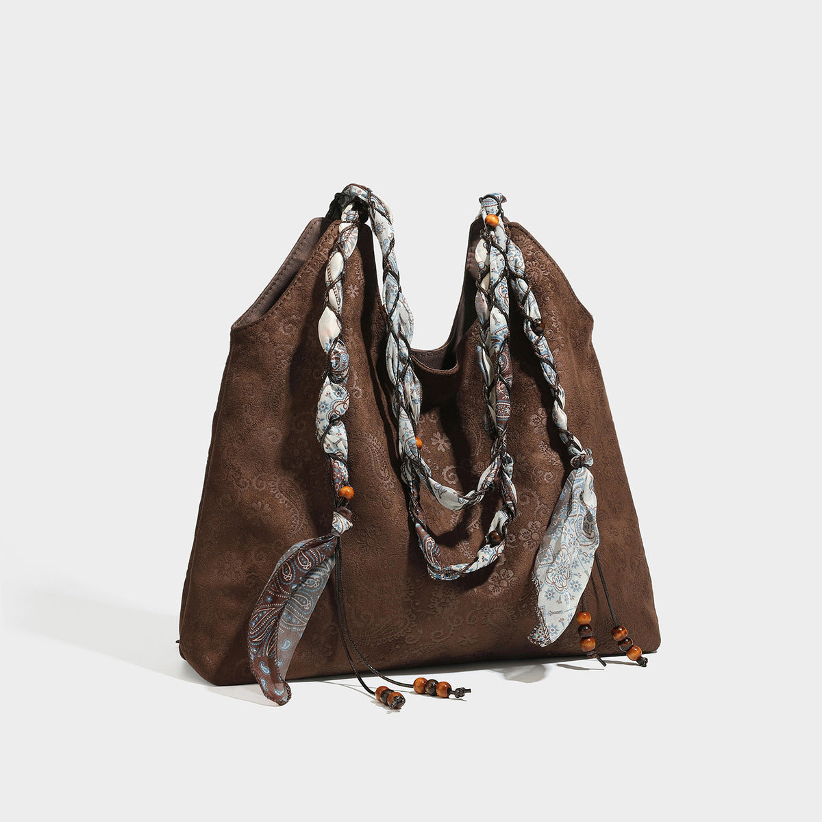 Slouchy paisley-embossed suede-look shoulder tote bag with braided patterned fabric straps and wood bead accents, detail view