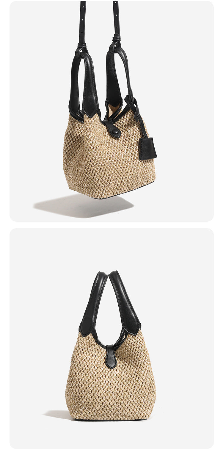 Woven beige straw bucket bag with black leather-look trim, dual top handles, detachable shoulder strap, and front snap