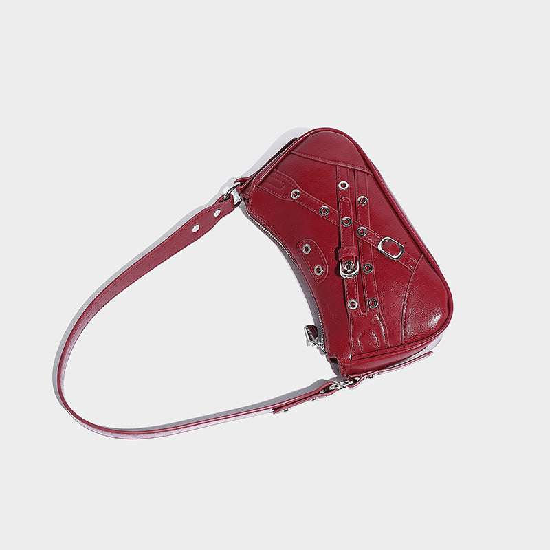 Compact moto-inspired shoulder bag with crisscross grommet strap detail, glossy textured finish, and adjustable crossbody