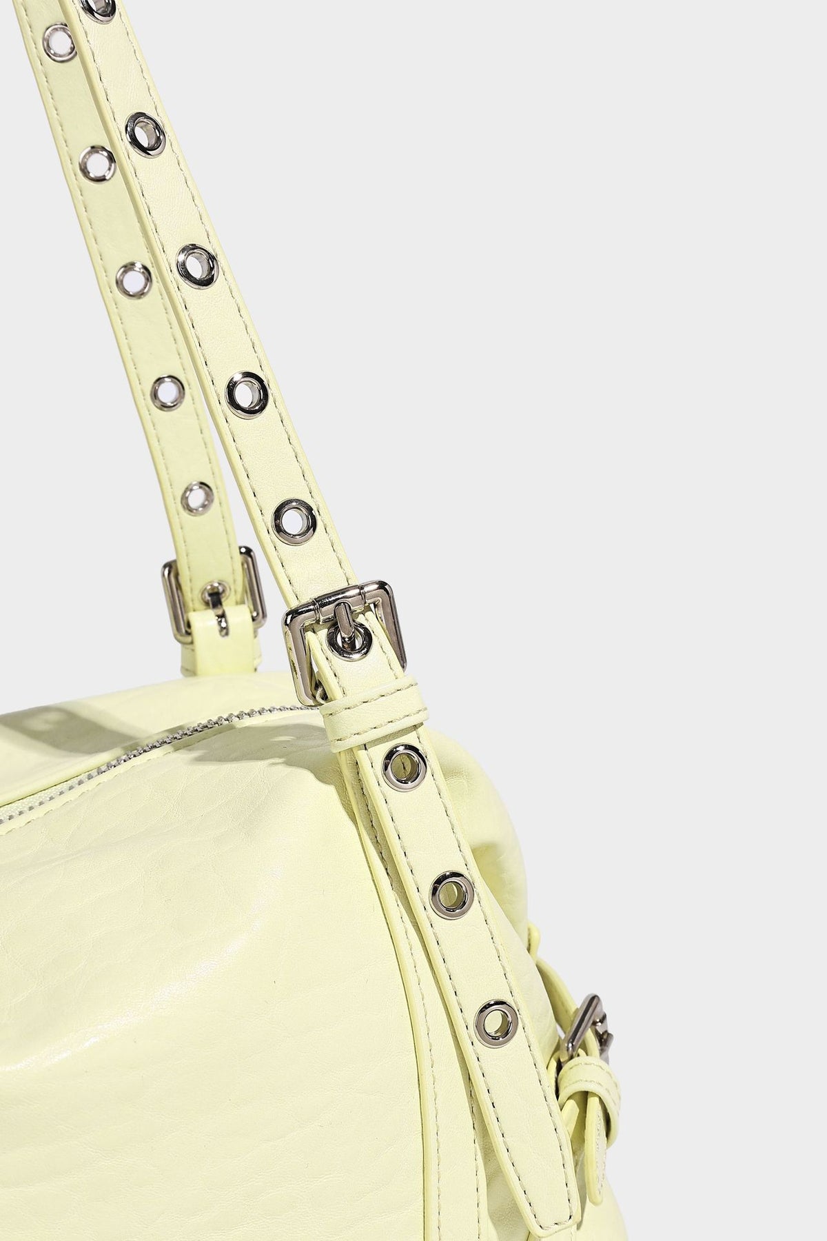Pale yellow leather-look barrel bag with silver grommet-studded shoulder straps, top zip closure, and pink tulip floral