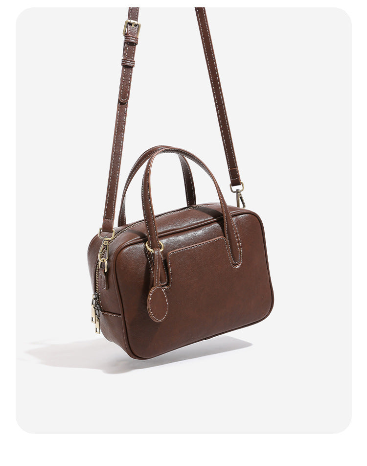 Structured boxy bowling-style tote bag in deep brown leather-look finish with dual top handles, front slip pocket, round