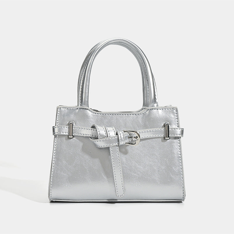 Small structured trapezoid mini top-handle bag with front belt-knot buckle detail and glossy leather-look finish, detail view