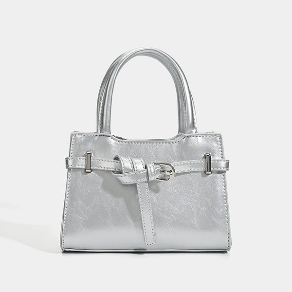 Small structured trapezoid mini top-handle bag with front belt-knot buckle detail and glossy leather-look finish, detail view