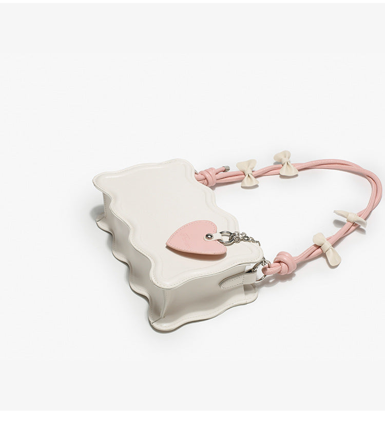 Small structured scalloped-edge shoulder bag with bow-tied pink cord strap and silver heart charm pendant, detail view 9