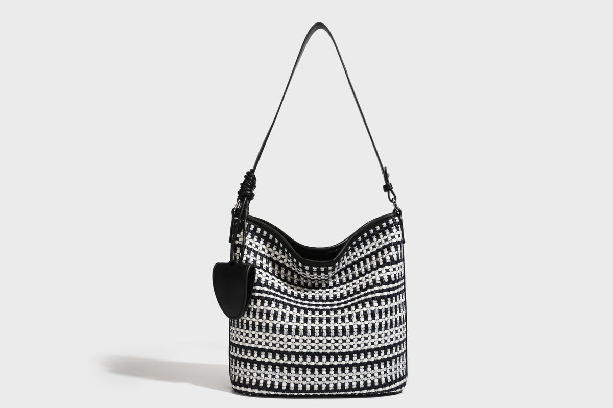Woven stripe bucket shoulder bag in cream and dark brown with leather-look trim, knotted adjustable strap, and small shield