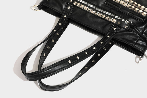 Black leather-look tote bag with silver pyramid studs on handles and front panel, multiple flap and zip exterior pockets